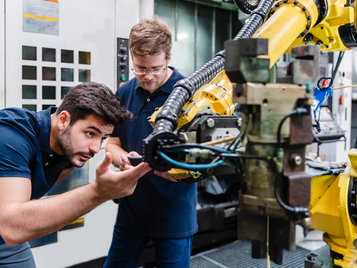 Two men inspecting a piece of machinery closely with one holding a tablet making notes.